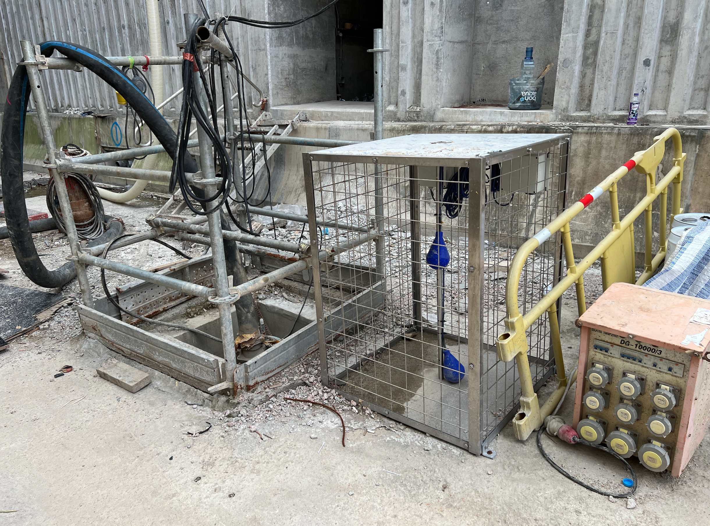 Water-level float sensors installed inside a stainless steel cage beside a construction site sump